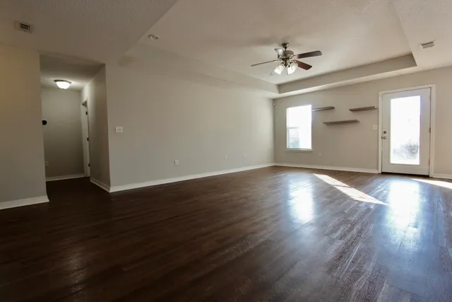 a view of an empty room with wooden floor and a ceiling fan