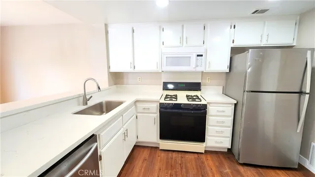 a kitchen with stainless steel appliances granite countertop a refrigerator stove a sink and white cabinets with wooden floor