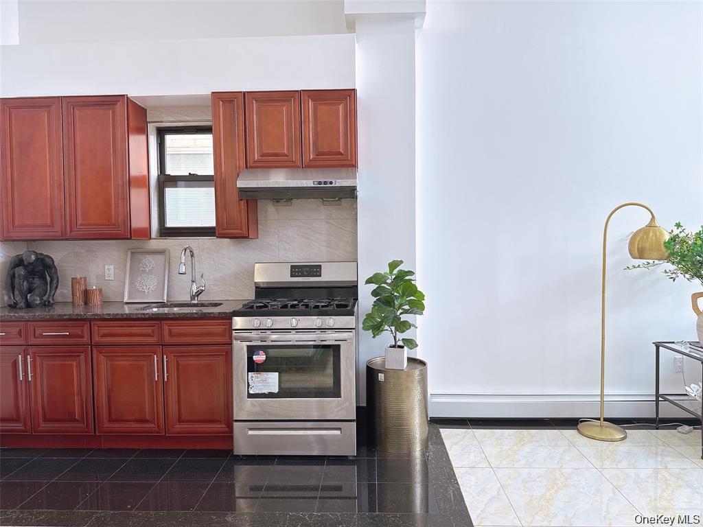 31-47 137th Street, Unit 4C Queens, NY 11354 - Photo 6 of 11 Kitchen with gas range, backsplash, under cabinet range hood, dark stone countertops, and reddish brown cabinets