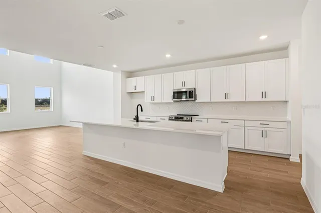a large white kitchen with wooden floors stainless steel appliances and white cabinets