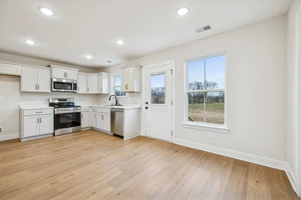 a kitchen with wooden floors white cabinets appliances and a window