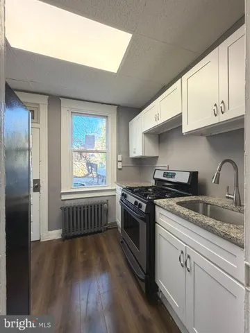 a kitchen with stainless steel appliances granite countertop a stove a sink dishwasher and white cabinets with wooden floor