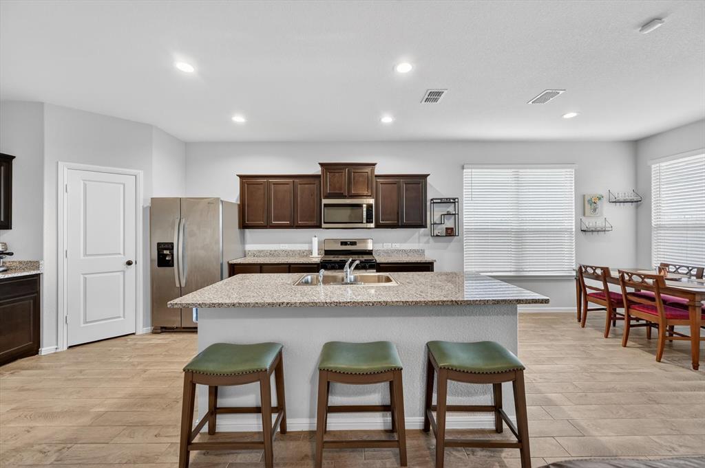 9604 Cherryville Road Fort Worth, TX 76108 - Photo 11 of 40 Open-concept kitchen featuring an island with a breakfast bar, recessed lighting, wood-finish flooring, dark wood cabinetry, and stainless steel appliances
