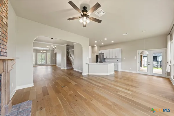 a view of an empty room and kitchen with wooden floor