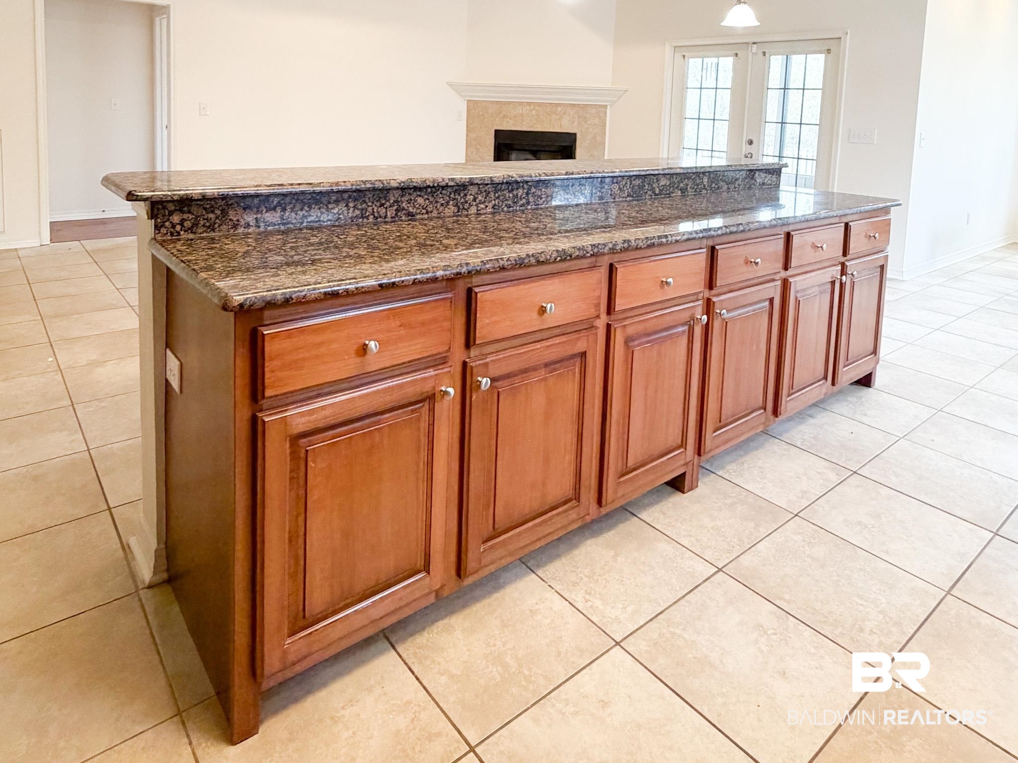 7332 Raintree Lane Gulf Shores, AL 36542 - Photo 8 of 21 Kitchen featuring wood finish cabinets, light tile patterned floors, a fireplace, dark stone countertops, and a kitchen island