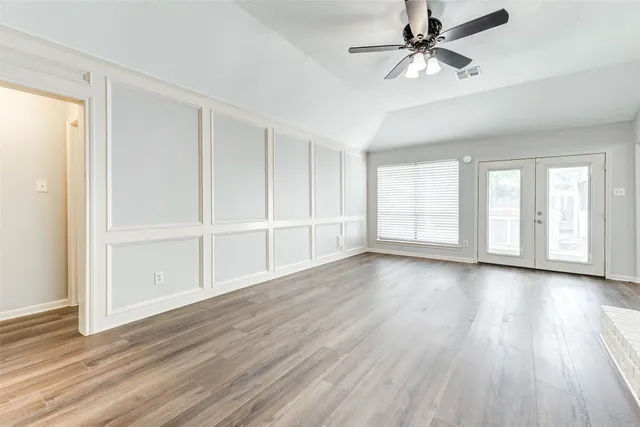 an empty room with wooden floor chandelier fan and windows