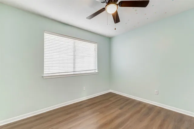 an empty room with wooden floor fan and windows