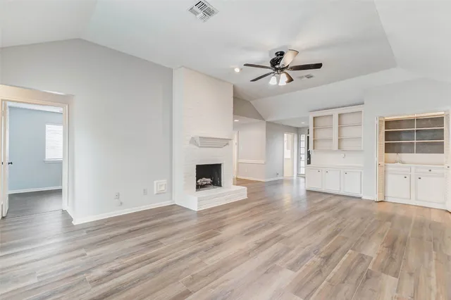 an empty room with wooden floor fireplace and windows