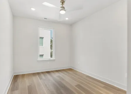 an empty room with wooden floor chandelier fan and windows