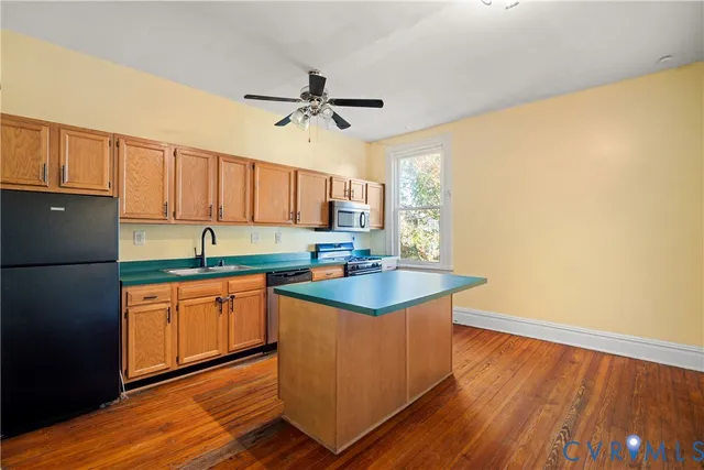 a kitchen with stainless steel appliances granite countertop a sink a stove a refrigerator cabinets and wooden floor