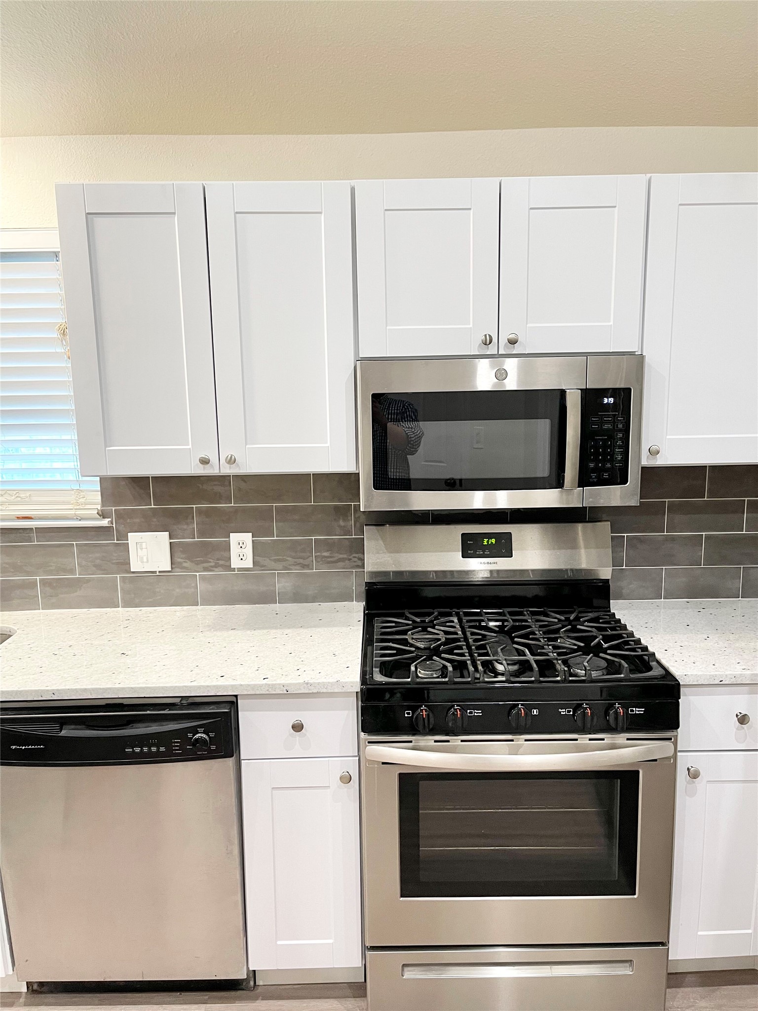 Kitchen with stainless steel appliances, light stone counters, white cabinetry, and tasteful backsplash