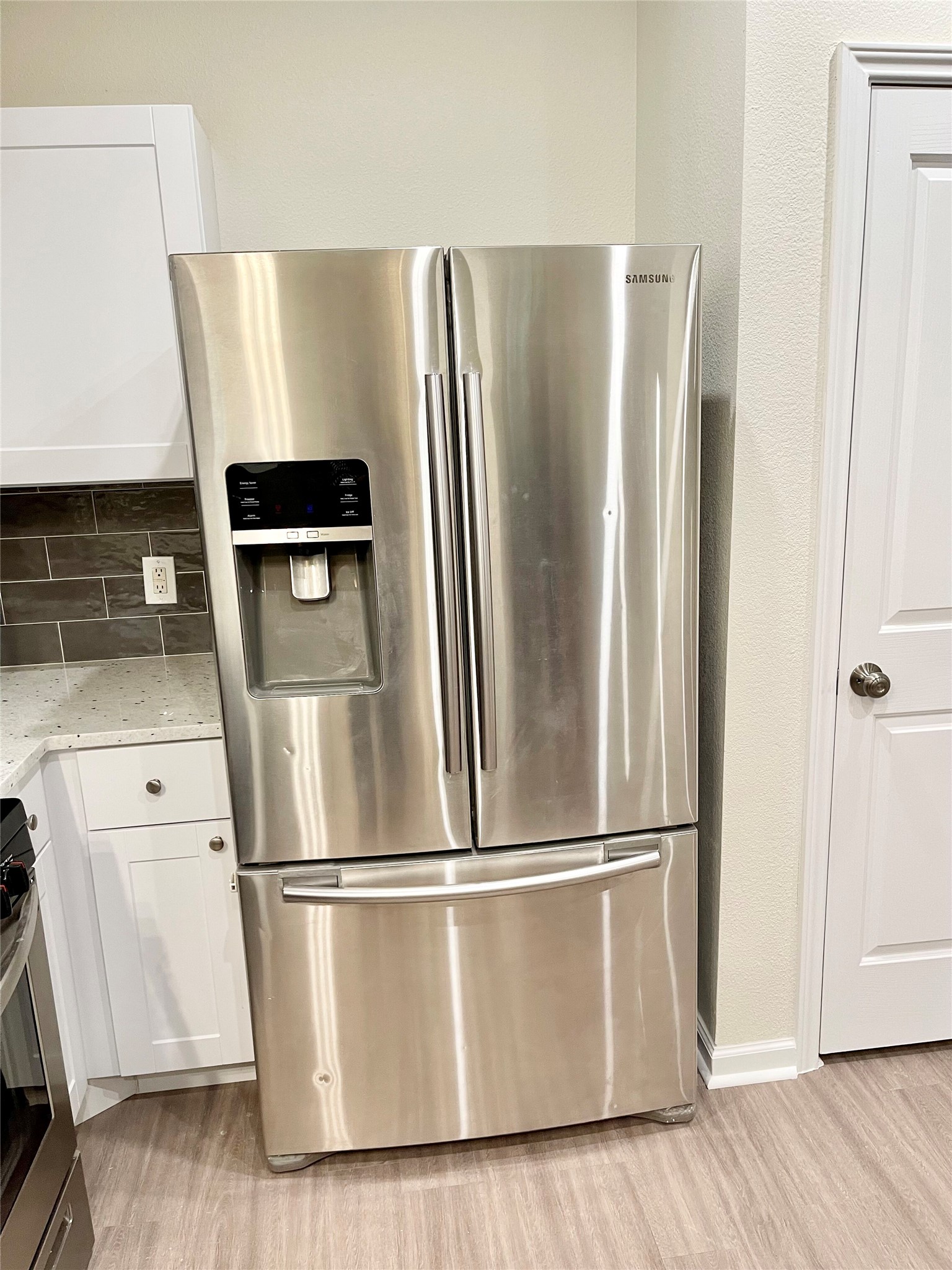 12513 Wethersby Way Austin, TX 78753 - Photo 4 of 16 Kitchen with stainless steel appliances, white cabinets, light stone countertops, light wood-style flooring, and decorative backsplash