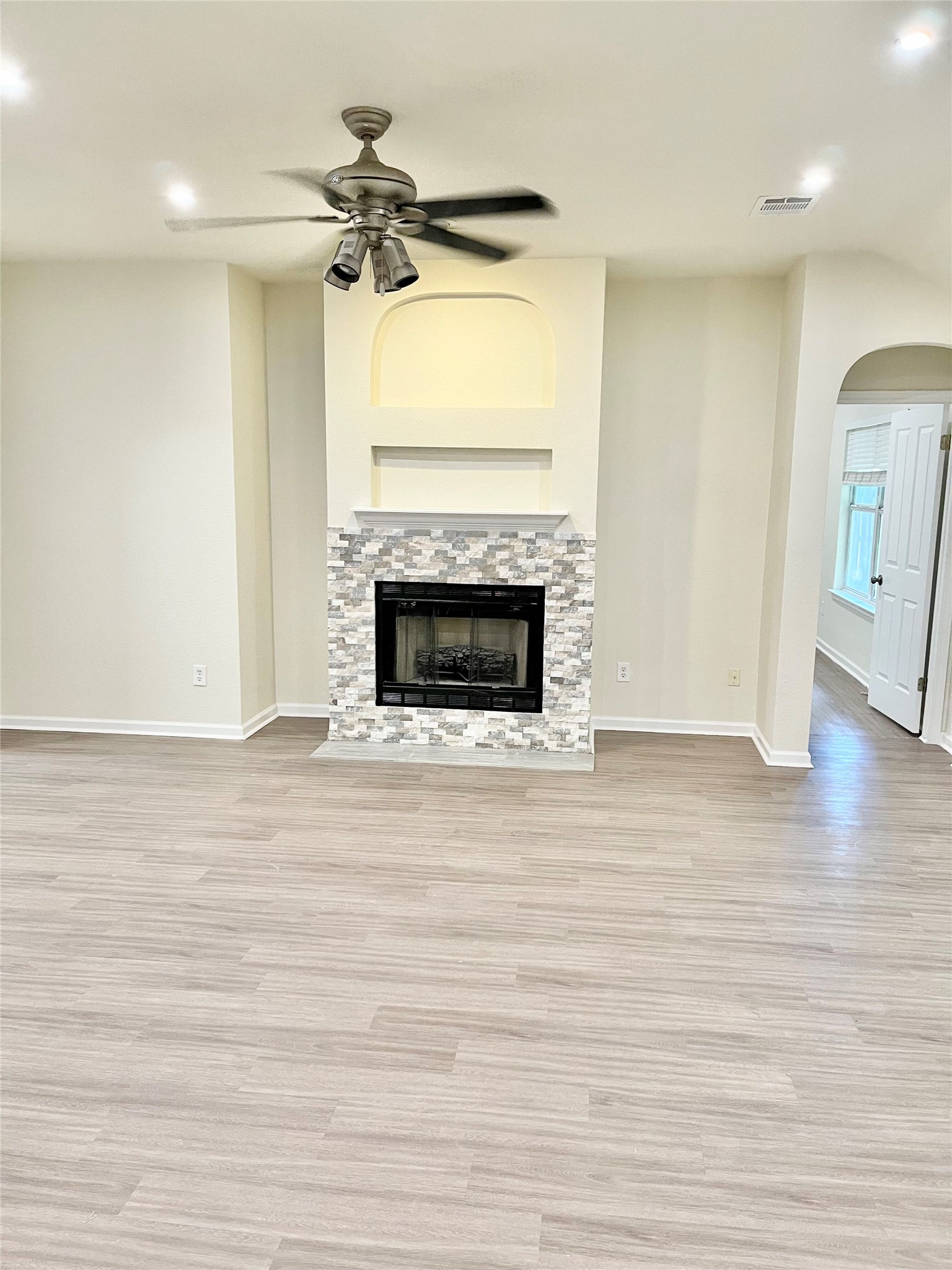 12513 Wethersby Way Austin, TX 78753 - Photo 6 of 16 Unfurnished living room featuring a ceiling fan, arched walkways, light wood-style floors, a stone fireplace, and recessed lighting
