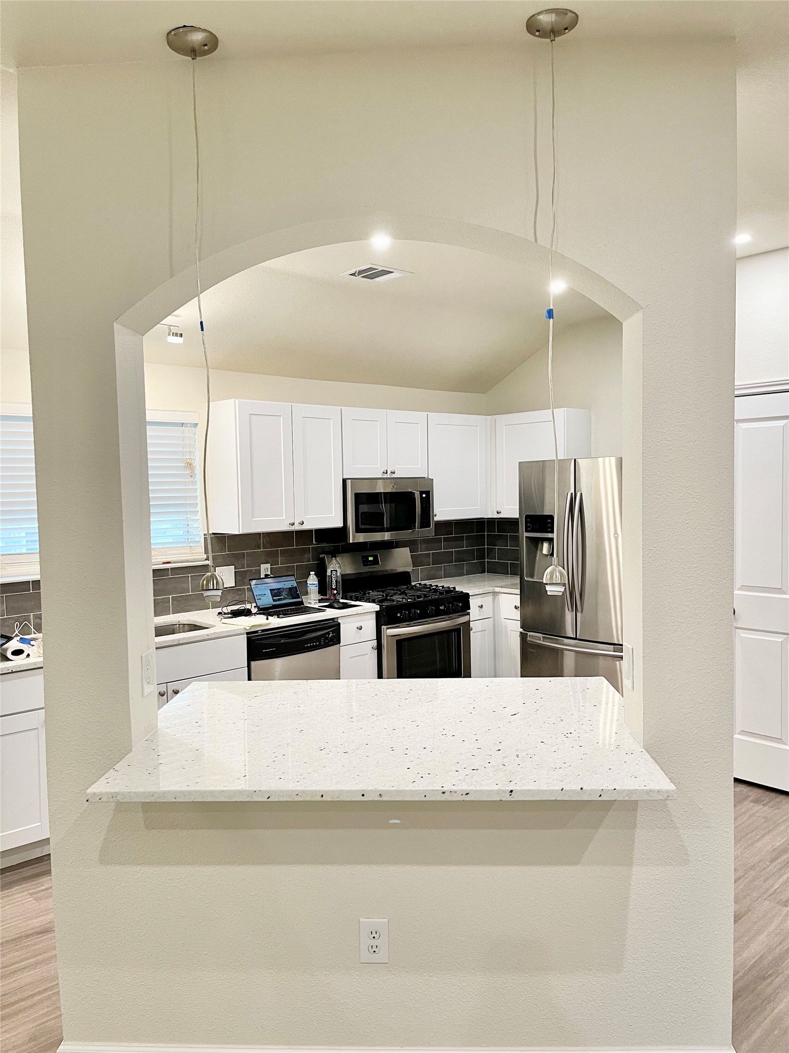 12513 Wethersby Way Austin, TX 78753 - Photo 8 of 16 Kitchen featuring light wood finished floors, white cabinets, stainless steel appliances, light stone counters, and arched walkways