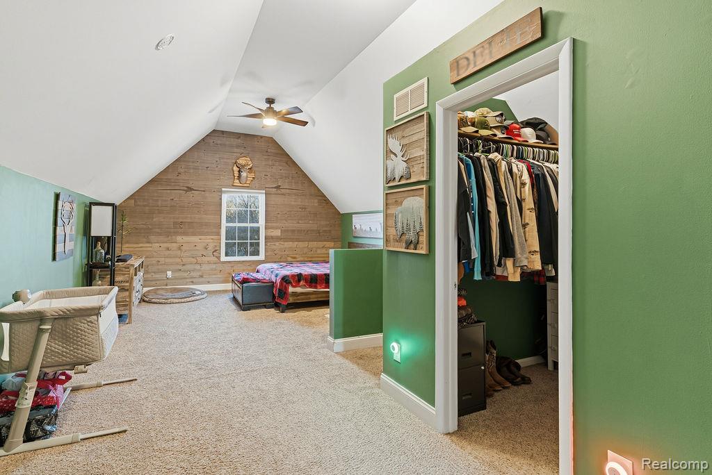 5216 South State Road Goodrich, MI 48438 - Photo 26 of 52 Carpeted bedroom featuring wooden walls, a spacious closet, vaulted ceiling, and ceiling fan