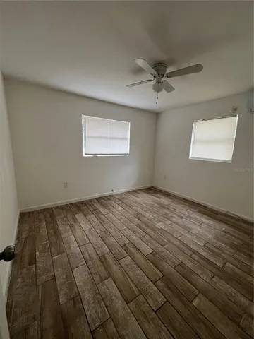 an empty room with wooden floor ceiling fan and windows