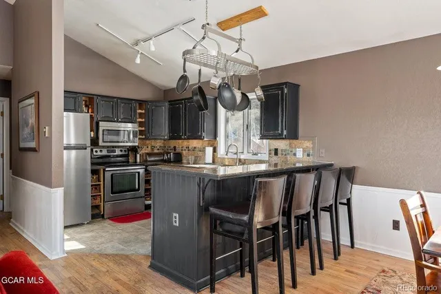 a kitchen with stainless steel appliances granite countertop a sink a stove a refrigerator cabinets and chairs