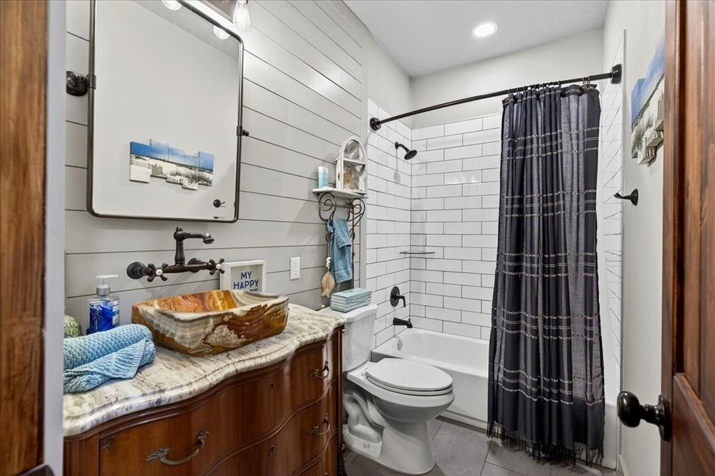 11591 Farm To Market 59 Athens, TX 75751 - Photo 20 of 40 Hall Bathroom on Level 1 featuring a unique natural stone vessel sink, wall-mounted faucet, and a vanity with a light-colored countertop, shiplap accent wall, subway tile in shower/tub, gray tile floor.