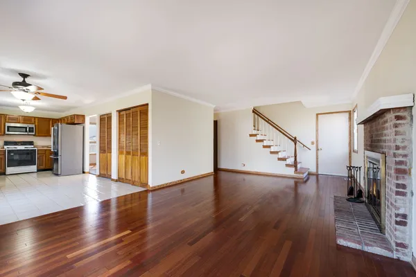 a view of an empty room with wooden floor stairs and a living room