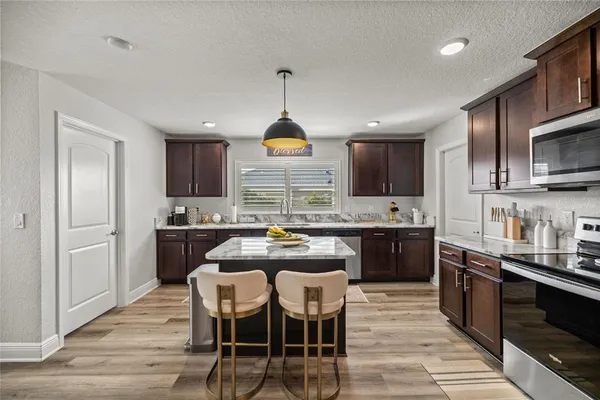 a kitchen with stainless steel appliances kitchen island granite countertop a stove top oven a sink dishwasher a dining table and chairs with wooden floor