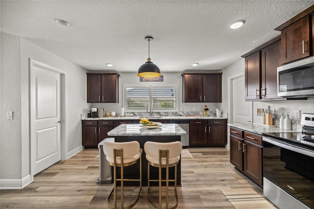 4160 Southwest 100th Street Ocala, FL 34476 - Photo 20 of 42 a kitchen with stainless steel appliances kitchen island granite countertop a stove top oven a sink dishwasher a dining table and chairs with wooden floor