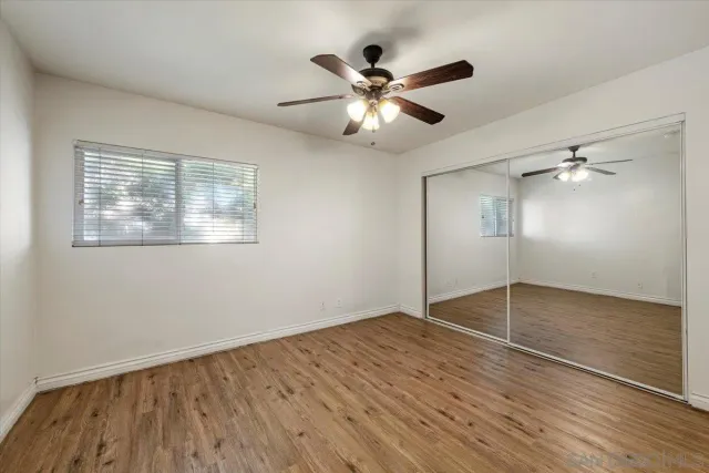 an empty room with wooden floor fan and windows