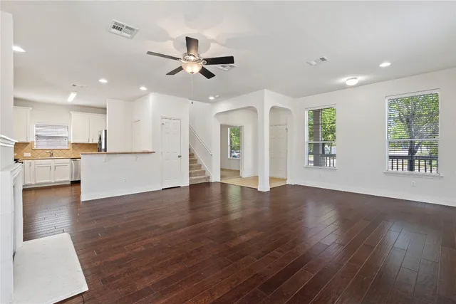 a view of an empty room and kitchen with wooden floor and a window