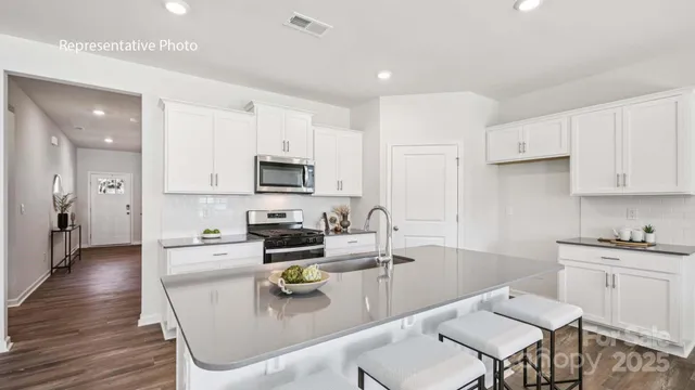 a kitchen with stainless steel appliances granite countertop a sink dishwasher a stove a refrigerator a microwave oven with white cabinets and wooden floor