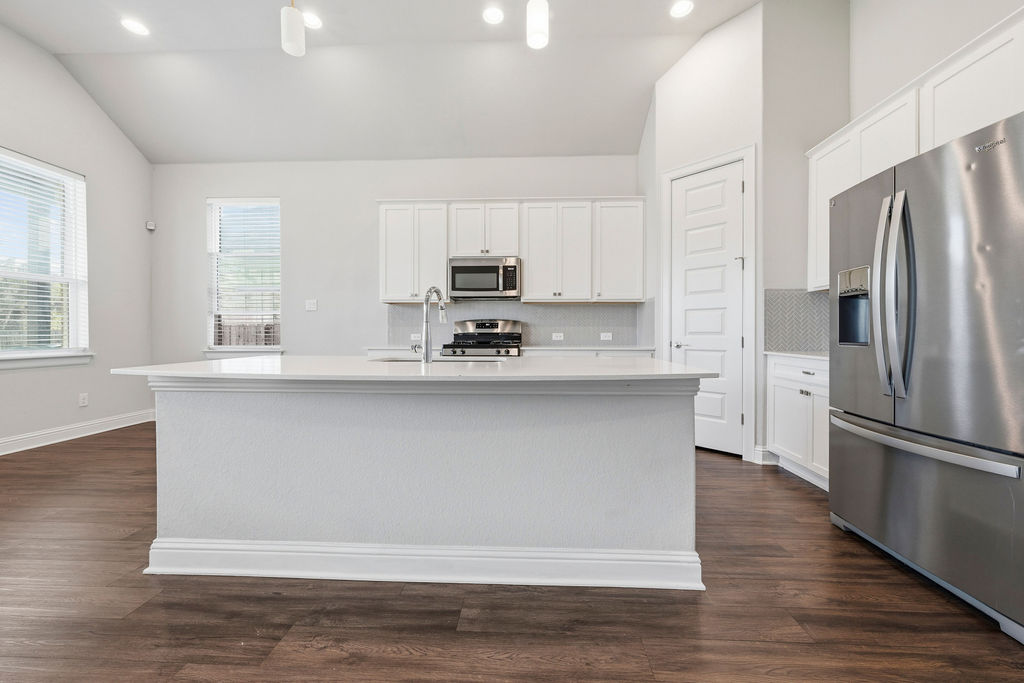 2032 Base Burner Path Leander, TX 78641 - Photo 7 of 34 Kitchen featuring a central island with an undermount sink, stainless steel appliances, white cabinetry, herringbone tile backsplash, and wood-finish flooring