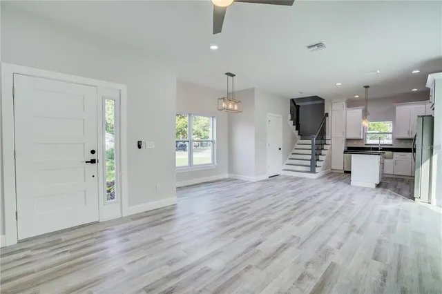 an empty room with wooden floor kitchen view and windows