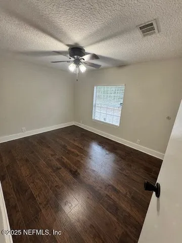 an empty room with wooden floor ceiling fan and windows