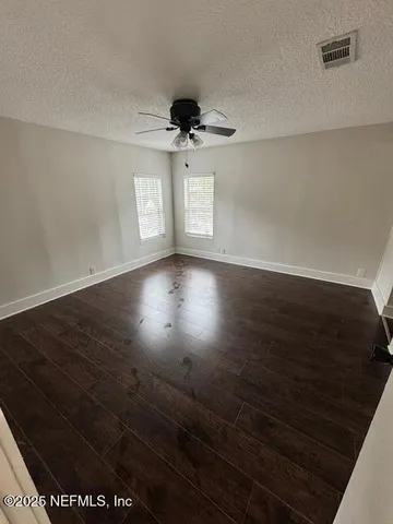 an empty room with wooden floor chandelier fan and windows
