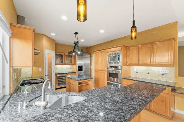 a kitchen with stainless steel appliances kitchen island granite countertop a refrigerator a stove and white cabinets with wooden floor