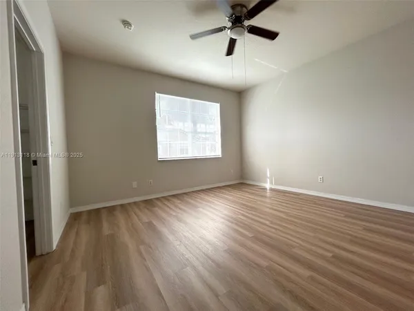 an empty room with wooden floor fan and windows