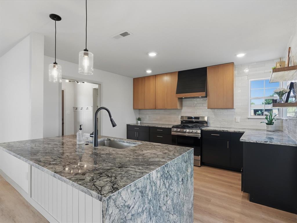 289 County Road 4655 Rhome, TX 76078 - Photo 1 of 34 Kitchen featuring a large island with a natural stone countertop and integrated sink, dual pendant lighting, wood-finish flooring, stainless steel range, and two-tone cabinetry