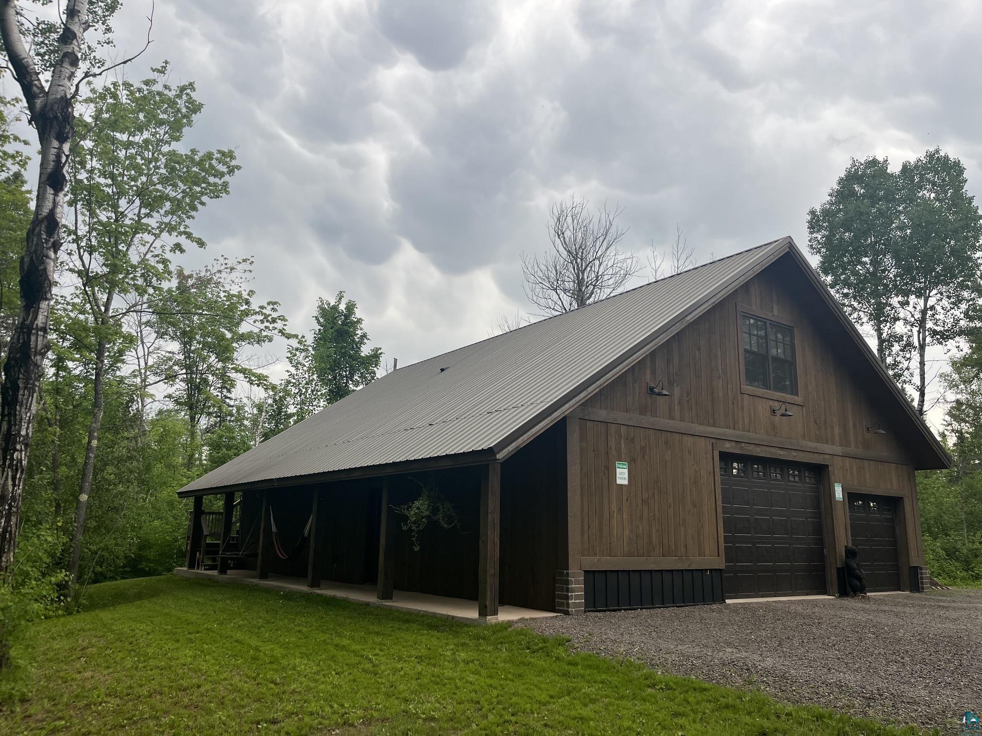 70745 Range Line Road Iron River, WI 54847 - Photo 36 of 40 Wood-clad structure with a metal roof, featuring a covered porch, two garage doors, and a gravel driveway