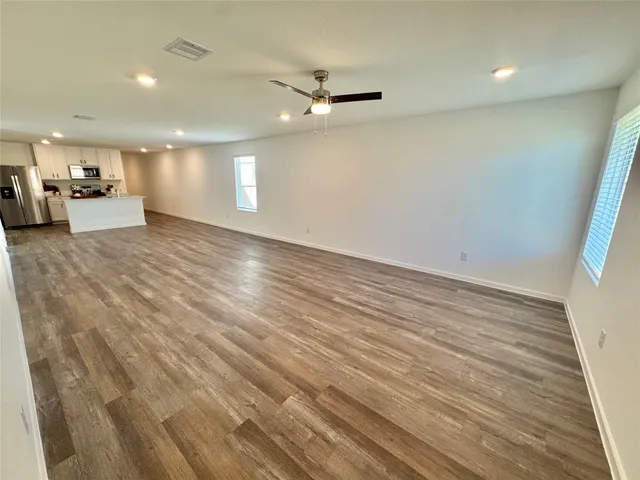 an empty room with wooden floor a ceiling fan and kitchen view