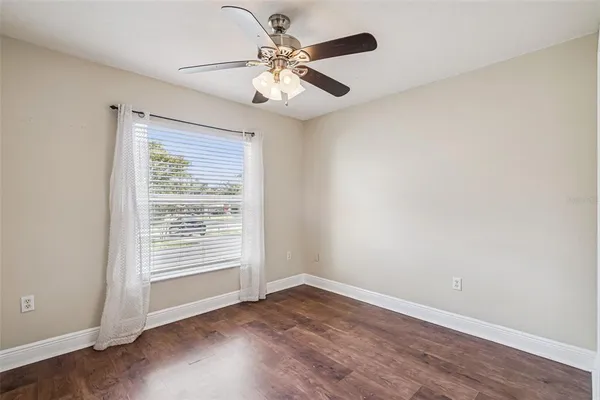 an empty room with wooden floor chandelier fan and windows