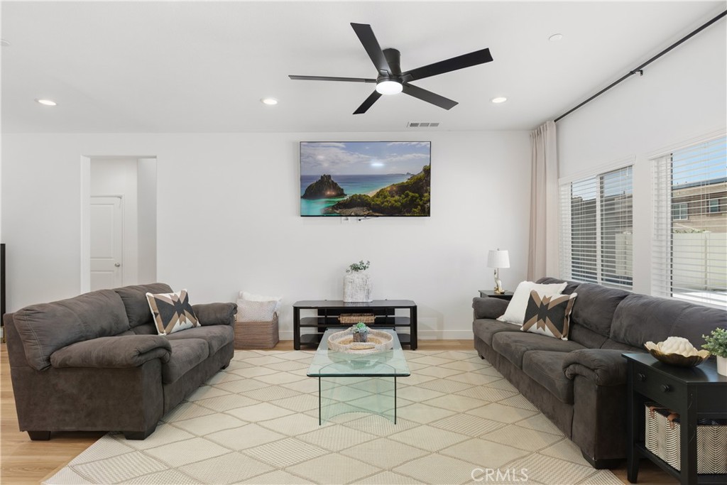 34727 Ribbon Grass Way Murrieta, CA 92563 - Photo 9 of 54 Sun-filled great room featuring wide-plank natural tone laminate flooring, sleek black modern fan, and oversized picture windows that create a light, airy feel, complemented by black curtain rods and linen drapery