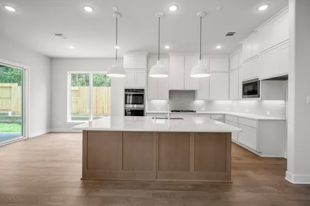 a kitchen with stainless steel appliances granite countertop a sink a microwave oven a refrigerator and white cabinets with wooden floor