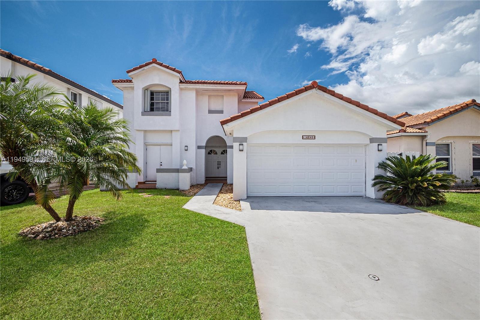 a view of a white house next to a yard with potted plants and large trees
