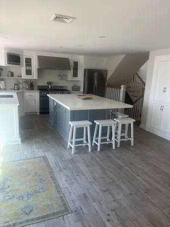 a white kitchen with stainless steel appliances granite countertop a stove a sink dishwasher a microwave oven and a dining table with wooden floor
