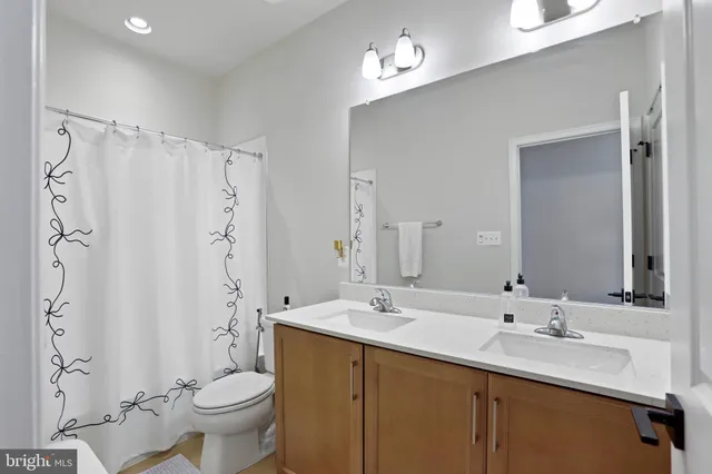 a bathroom with double vanity sink a toilet a mirror and shower
