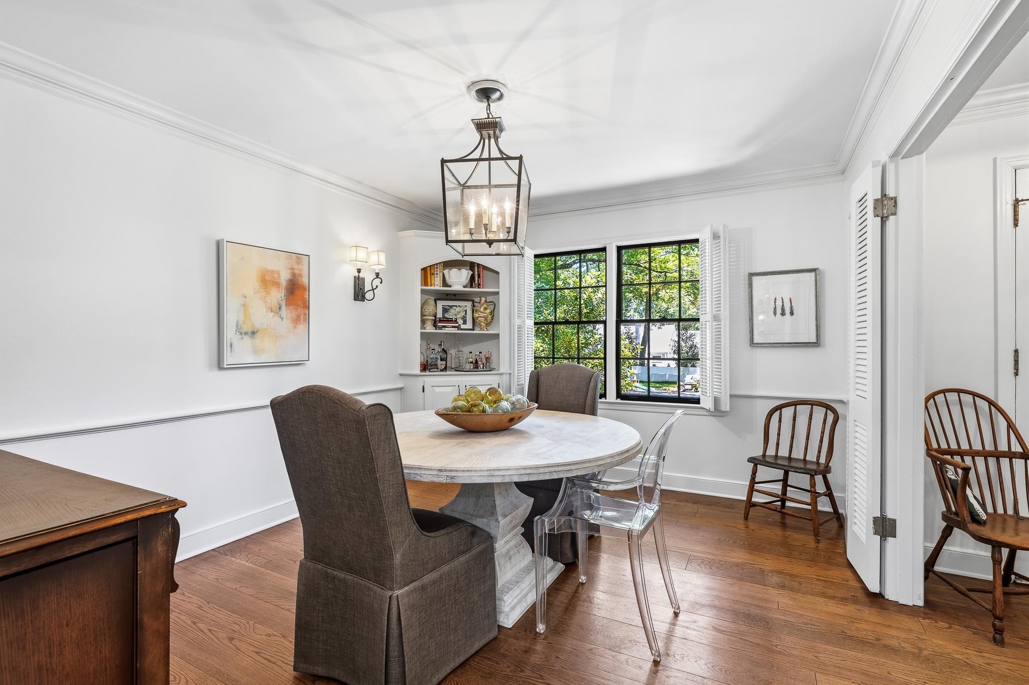 Dining space featuring hardwood flooring, white wainscoting, and a built-in corner cabinet with shelving