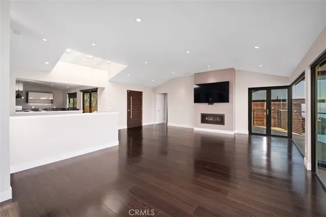 a view of an empty room with wooden floor and a kitchen