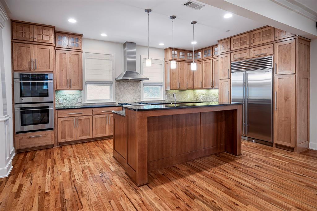 a kitchen with kitchen island granite countertop wooden floors stainless steel appliances a sink and a counter space