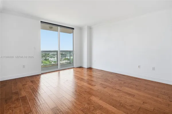 a view of an empty room with wooden floor and a window