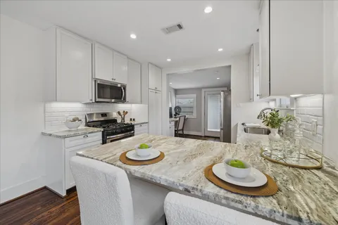 a kitchen with stainless steel appliances granite countertop a stove a sink a refrigerator and a white cabinets