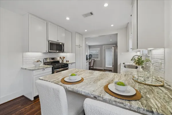 a kitchen with stainless steel appliances granite countertop a stove a sink a refrigerator and a white cabinets