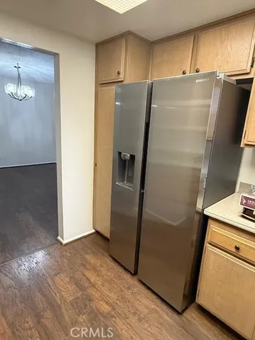 a view of a refrigerator in kitchen and an empty room with wooden floor